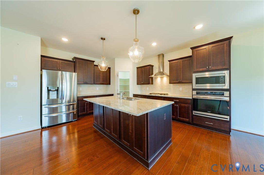 Kitchen featuring a central island with a stone countertop, dark wood-finish cabinetry, stainless steel appliances, and wood-finish flooring