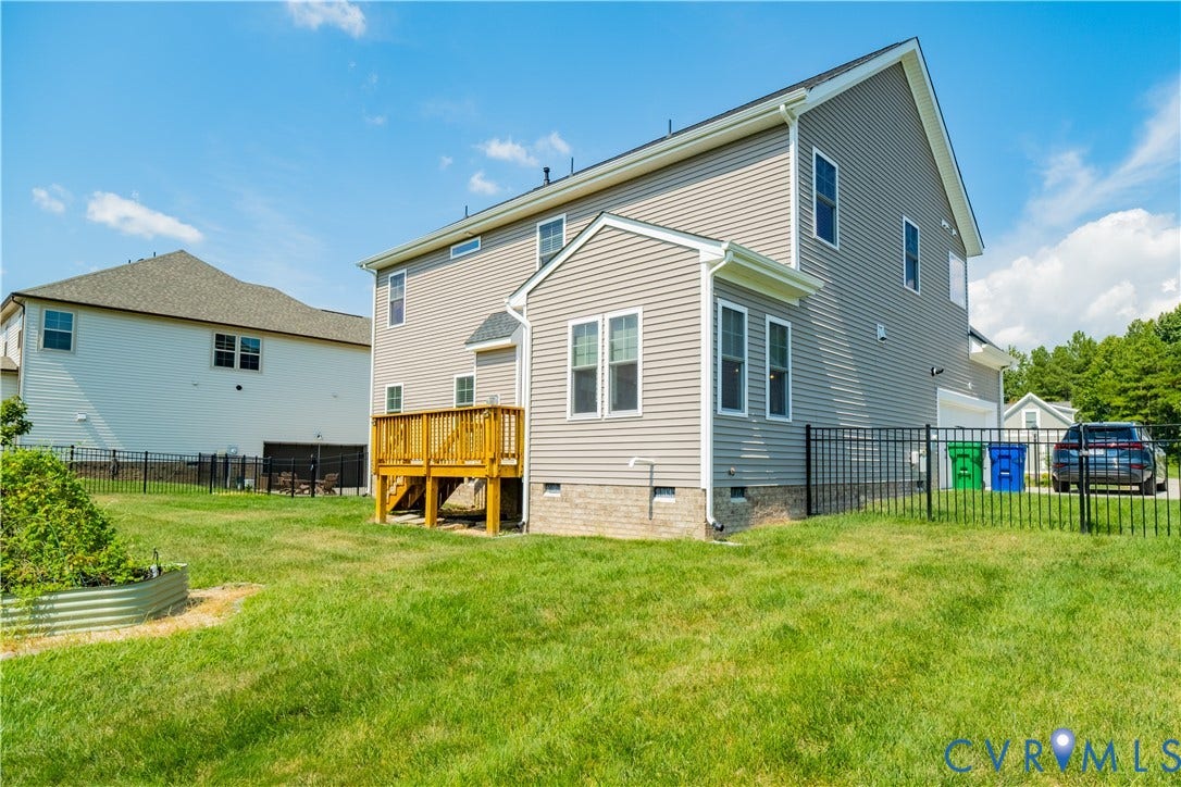 Rear exterior with a wooden deck, gray siding, and a black metal fence