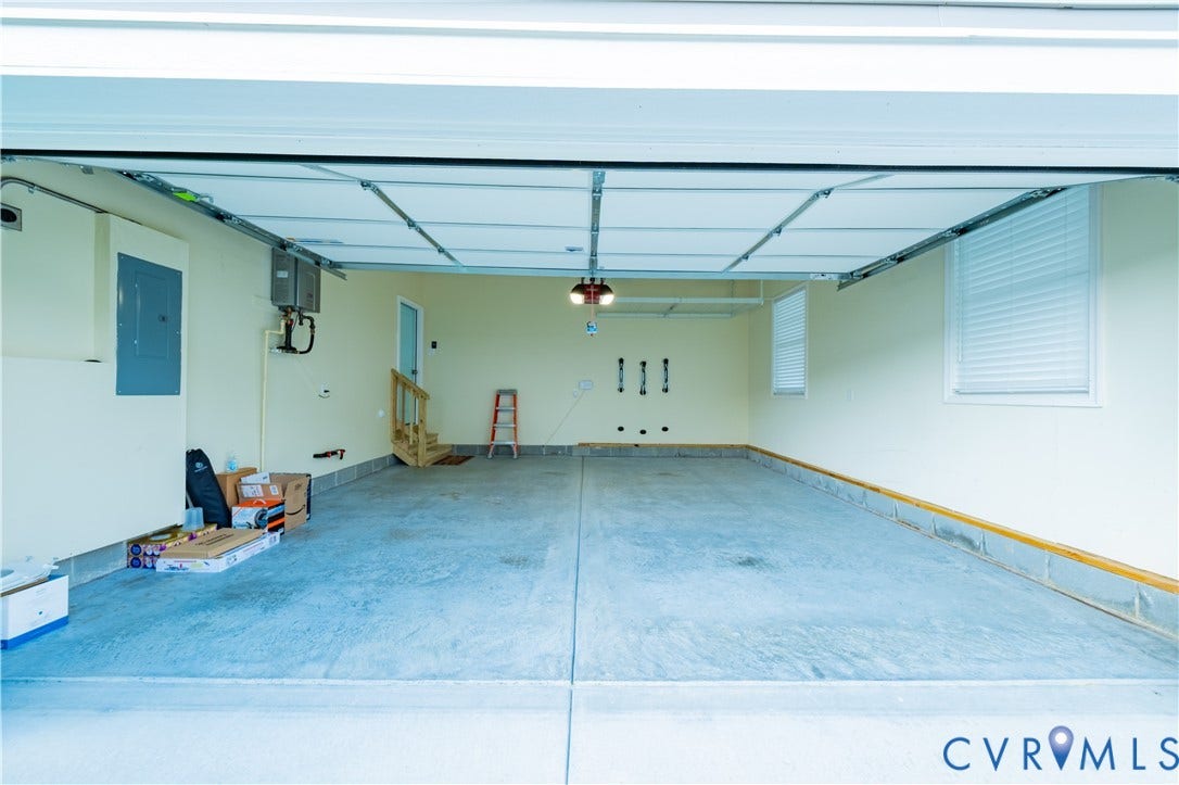 Spacious garage with a concrete floor, overhead lighting, two windows with blinds, and a built-in staircase