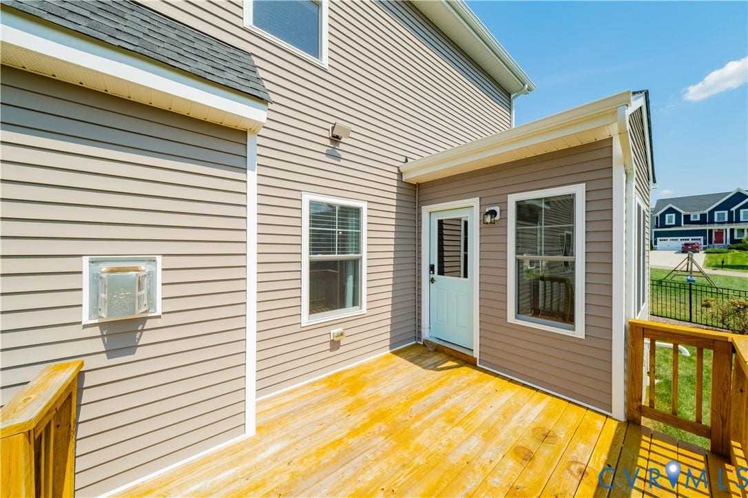 Expansive wood deck with wood railings, a light-colored entry door, and exterior sconce lighting, all against neutral-toned siding