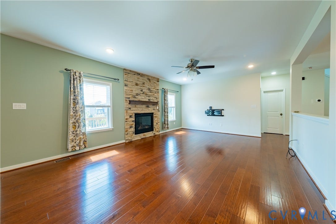 Spacious room featuring wood-finish flooring, a stone-clad fireplace, and recessed lighting