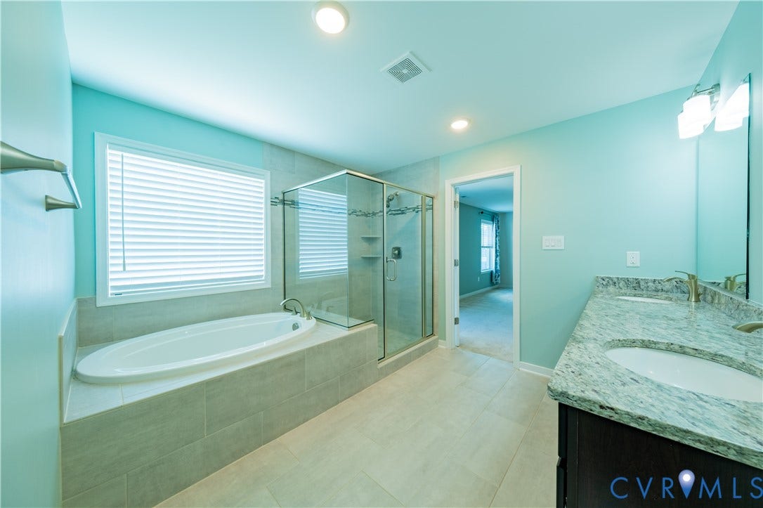 Tiled flooring, dual vanity with stone countertop, frameless glass shower enclosure, and a built-in bathtub with a tiled surround