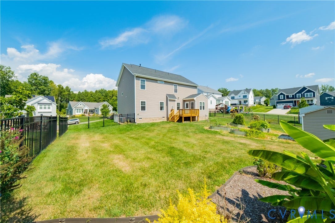 Expansive yard with green lawn, black metal fencing, wood deck, and raised garden beds