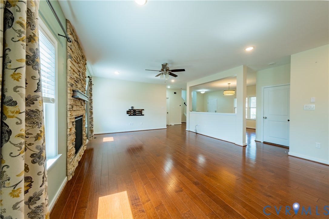 Spacious living area featuring wood-finish flooring, a stone-clad fireplace, and a ceiling fan