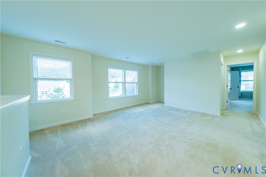 Expansive carpeted area featuring multiple windows with blinds, recessed lighting, and a white painted wall finish