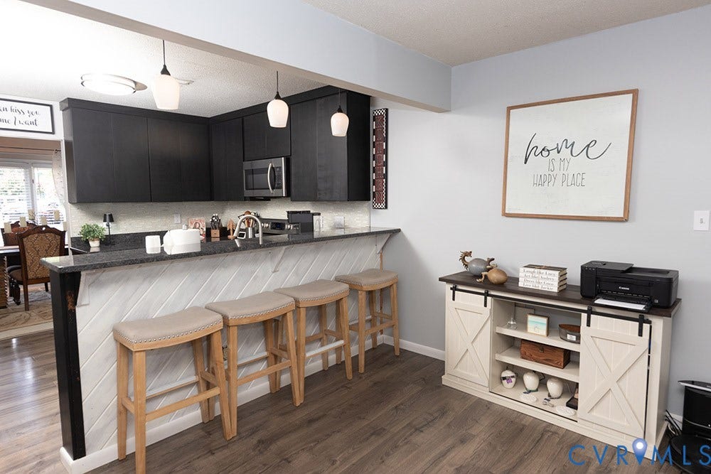 2209 Aspen Place, Henrico, VA 23233 Modern kitchen and entertaining space featuring black cabinetry with stainless steel appliances, quartz waterfall island countertop with seating for three, pendant lighting, and wood-finish flooring throughout