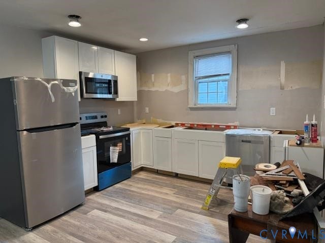 Kitchen featuring stainless steel appliances, white cabinetry, overhead lighting, and wood-finish flooring