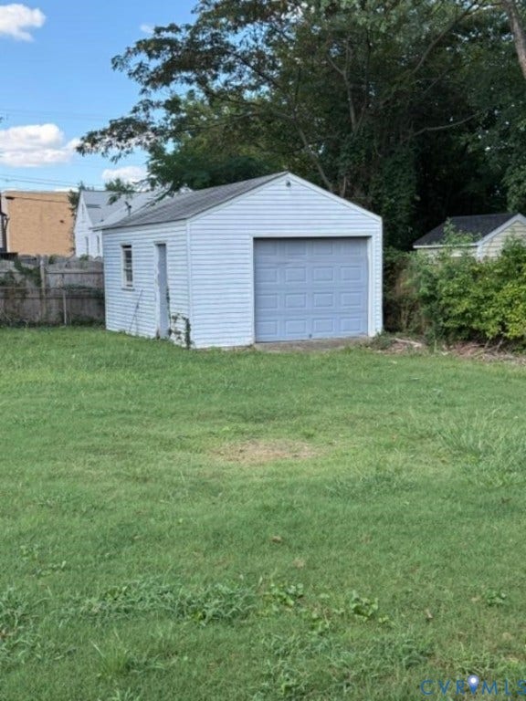 Detached garage with siding exterior and a gray overhead door, situated on a grassy lot