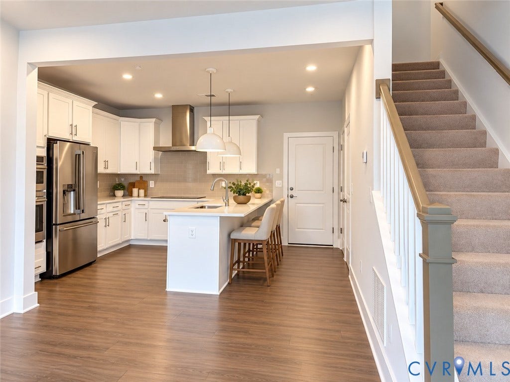 4113 Greybull Drive, #A, Gateway Square, Henrico, VA 23233 Virtually staged. Open-concept kitchen with wood-finish flooring, white cabinetry, stainless steel appliances, and an island with pendant lighting