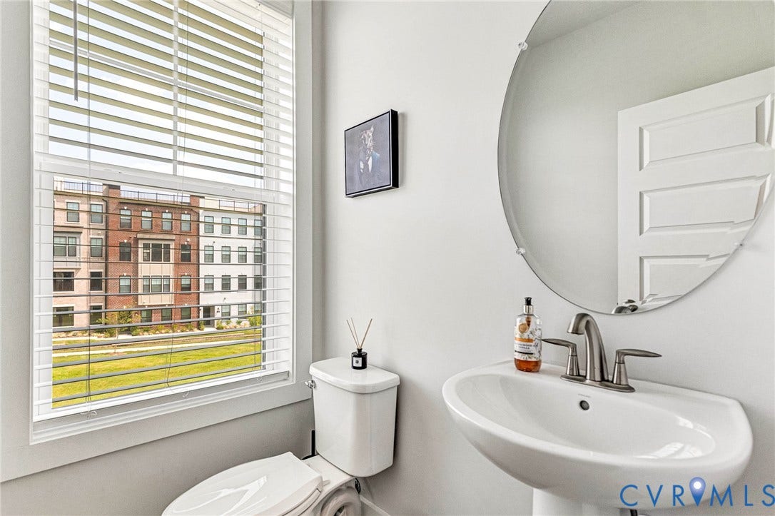 528 Greybull Walk, #B, Glen Allen, VA 23233 Pedestal sink with brushed nickel faucet, large oval frameless mirror, and a window with horizontal blinds