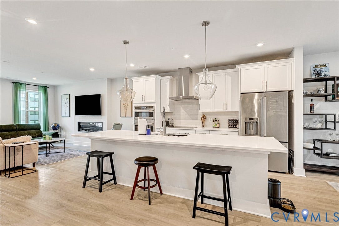 528 Greybull Walk, #B, Glen Allen, VA 23233 Open-concept kitchen and living area featuring wood-finish flooring, white cabinetry, a large kitchen island with pendant lighting, stainless steel appliances, and a built-in fireplace