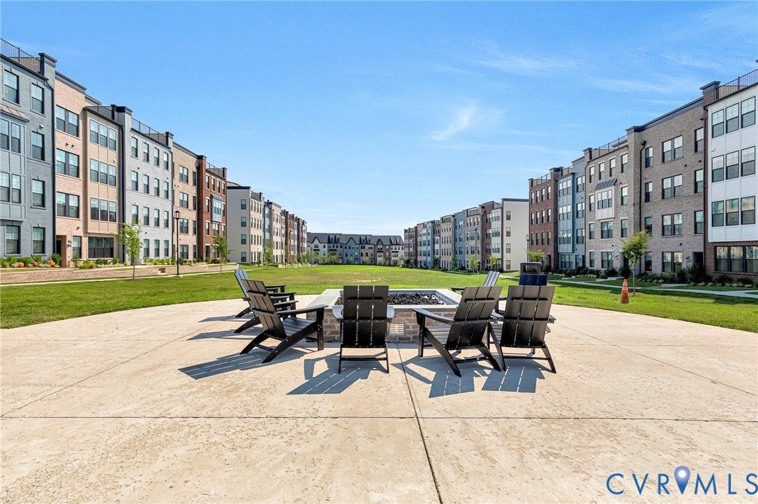 528 Greybull Walk, #B, Glen Allen, VA 23233 Concrete patio with a central fire pit feature, surrounded by expansive green lawn, and multi-story residential structures with varied facades