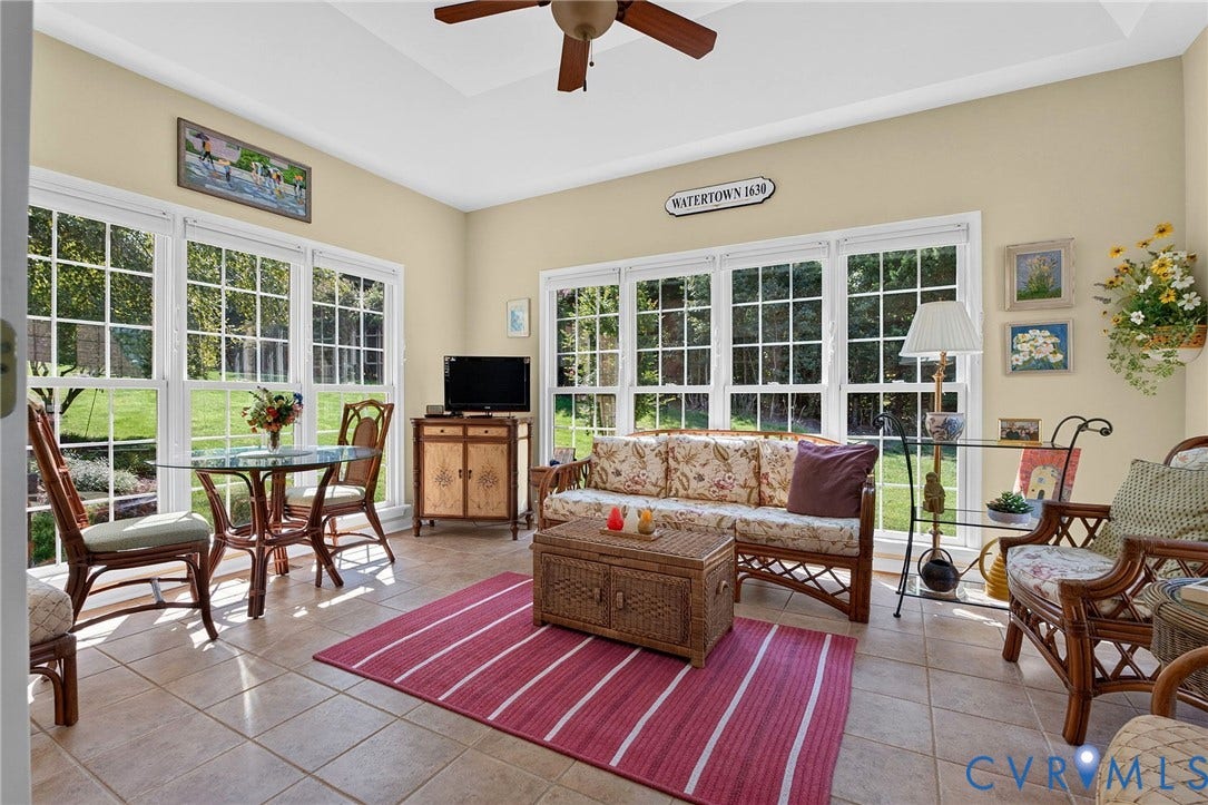 A bright, inviting sunroom surrounded by windows, with tile flooring and peaceful views of the lush, wooded backyard.