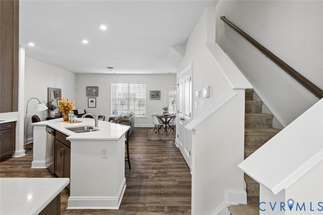 Open-concept living space with LVP flooring, a kitchen island with integrated sink, recessed lighting, and a prominent staircase with carpeting.