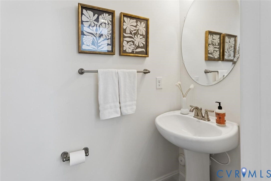 Pedestal sink with a brushed nickel faucet, wall-mounted oval mirror, and a coordinating towel bar