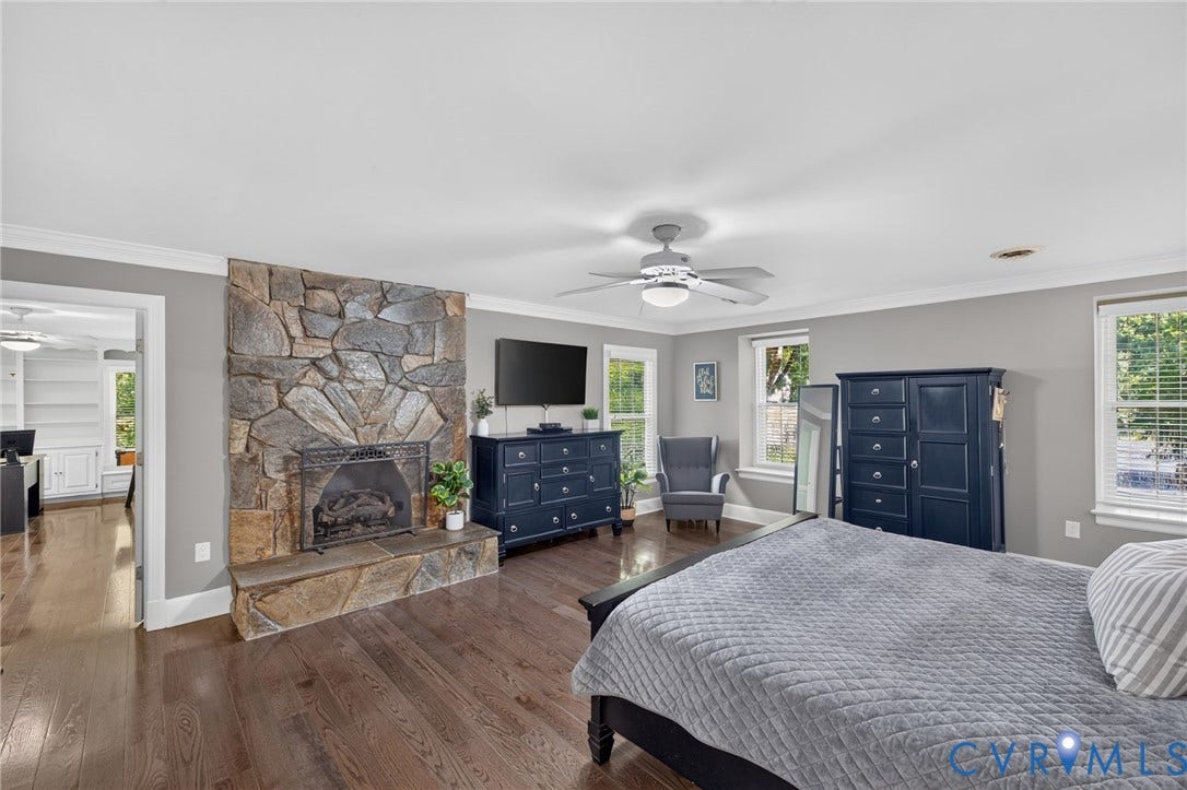 12800 Leffingwell Court, Henrico, VA 23233 Stone-clad fireplace feature with a hearth, dark wood-finish flooring, two windows with white blinds, and a ceiling fan with integrated lighting