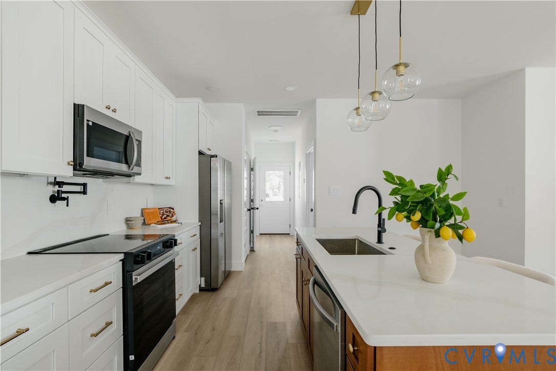 3106 Groveland Avenue, Richmond, VA 23222 Contemporary kitchen featuring stainless steel appliances, white cabinetry with brass-finish hardware, wood-finish flooring, and a center island with pendant lighting