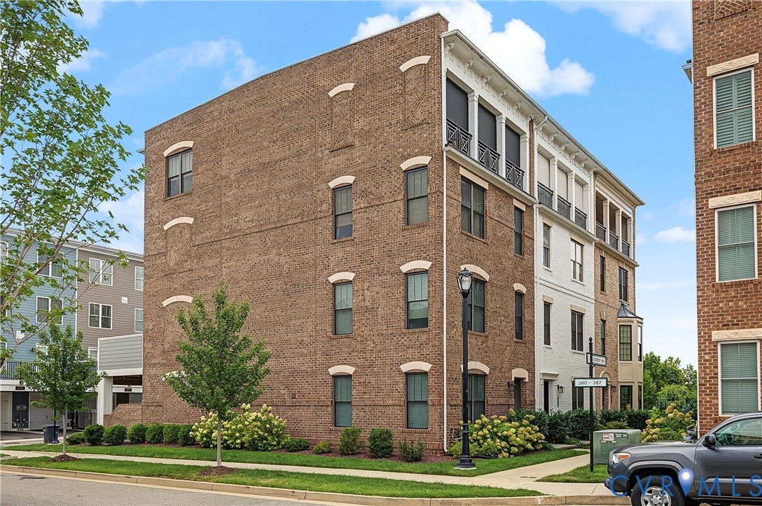 Brick exterior with decorative window arches, multiple balconies with metal railings, a bay window, and established landscaping