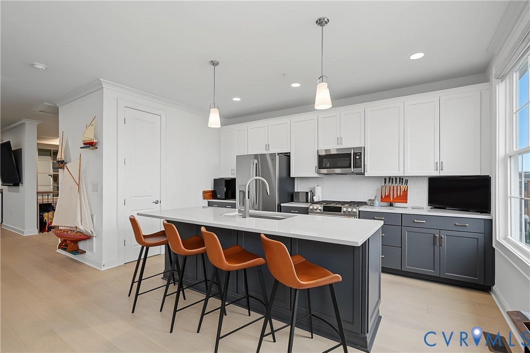Kitchen featuring a two-tone cabinetry design, stainless steel appliances, a center island with pendant lighting, and wood-finish flooring