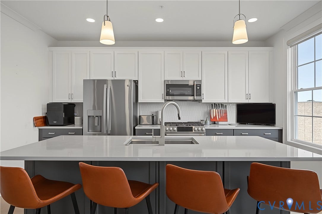 Kitchen featuring a center island, stainless steel appliances, white upper cabinetry, gray lower cabinetry, and a window with natural light