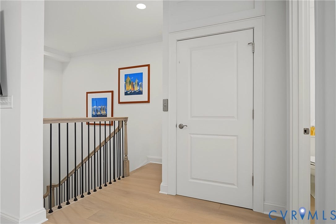 4th Level Landing Light wood-finish flooring, white paneled door, flush-mount ceiling lighting, and a staircase with black iron spindles and a natural wood handrail