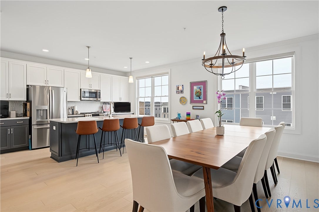 Light wood-finish flooring throughout, kitchen with white upper and dark lower cabinetry, stainless steel appliances, and a large island