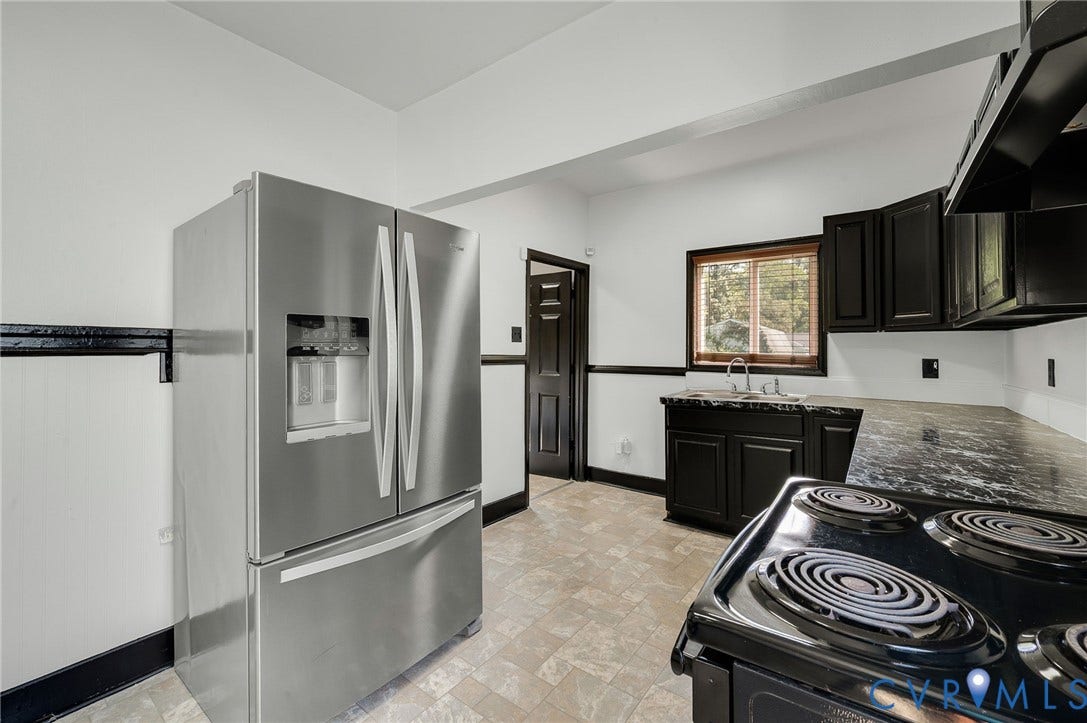 Kitchen featuring black cabinetry, a stainless steel refrigerator, black range, and stone countertops
