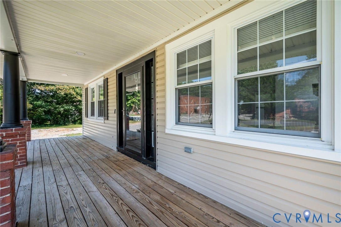 Expansive covered porch featuring wood-finish decking, brick and column supports, and dual glass paneled doors