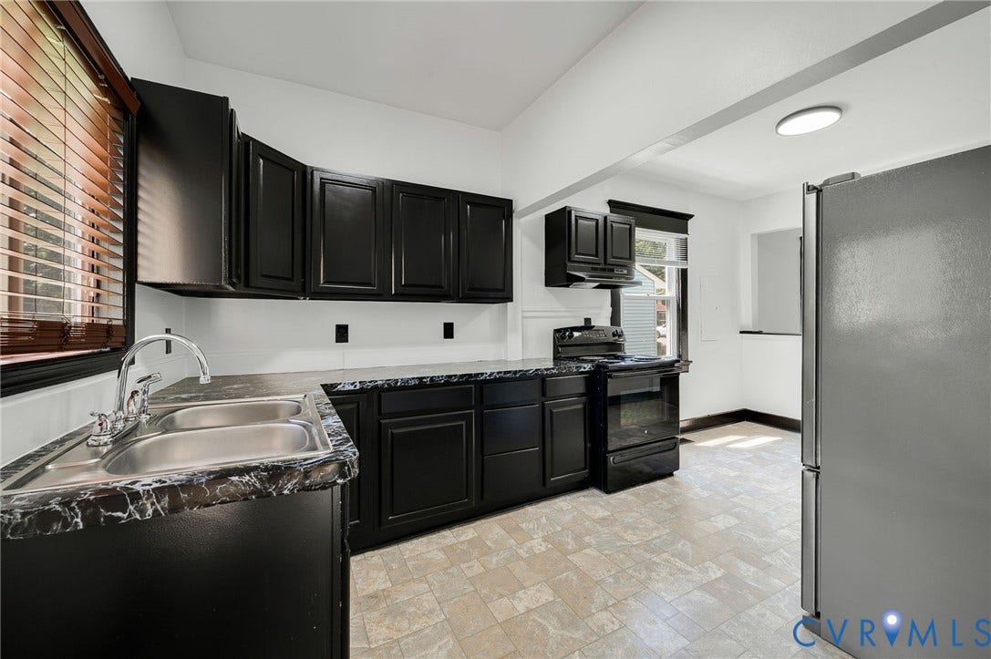 Kitchen featuring black cabinetry, double stainless steel sink, black countertops, and vinyl flooring