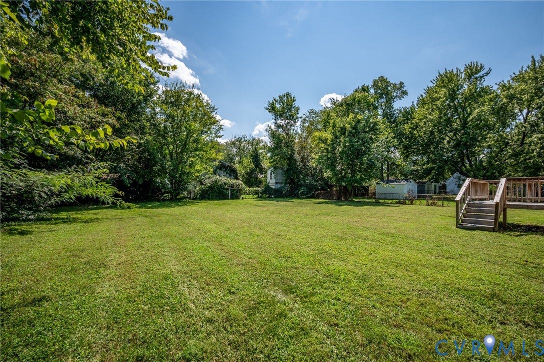 Expansive green lawn with mature perimeter trees and a multi-level wood deck