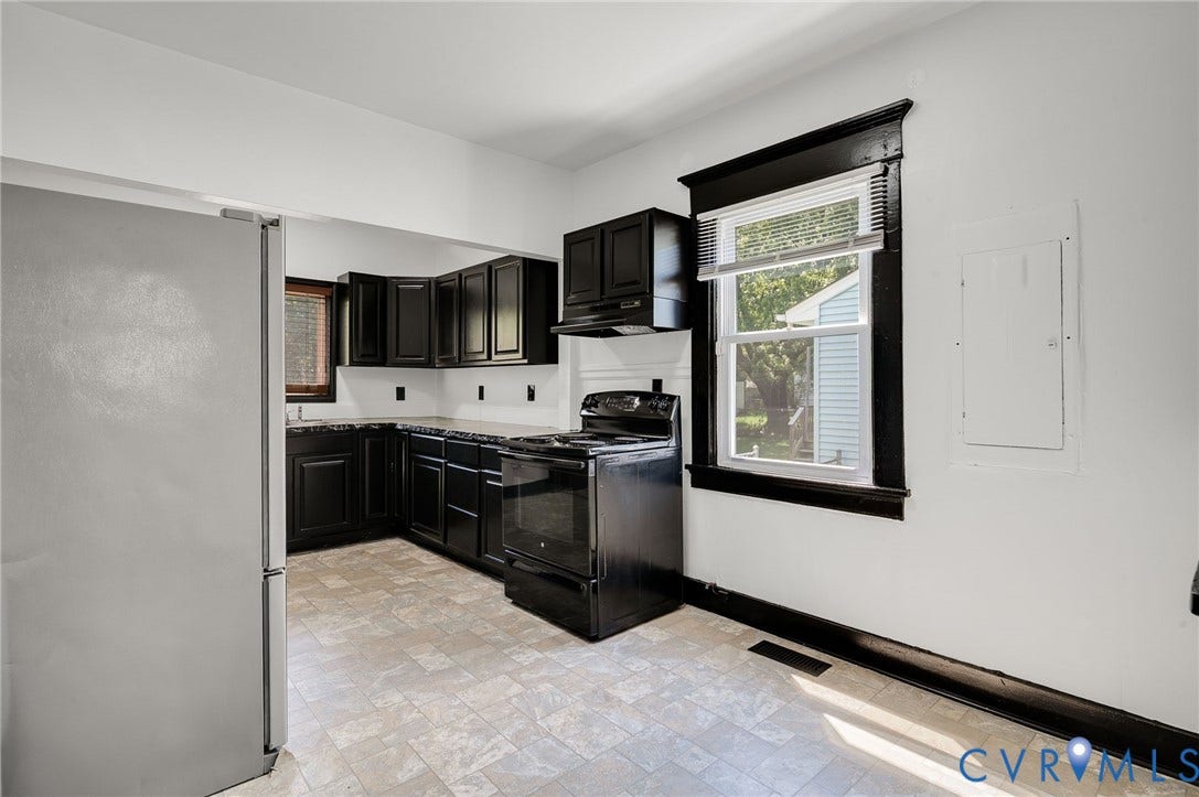 Kitchen featuring dark cabinetry, light-toned flooring, white walls, and a window with dark trim
