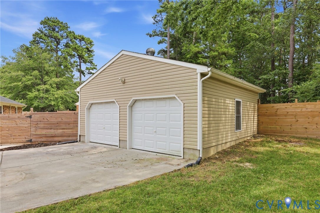 3221 Clintwood Road, Midlothian, VA 23112 Two-car garage with tan siding, dual white paneled garage doors, a concrete driveway, and a wooden privacy fence
