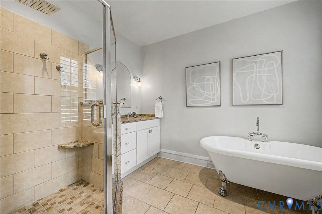 Walk-in shower with natural stone tile and built-in bench, freestanding clawfoot tub, single vanity with integrated sink and stone countertop, and neutral tile flooring