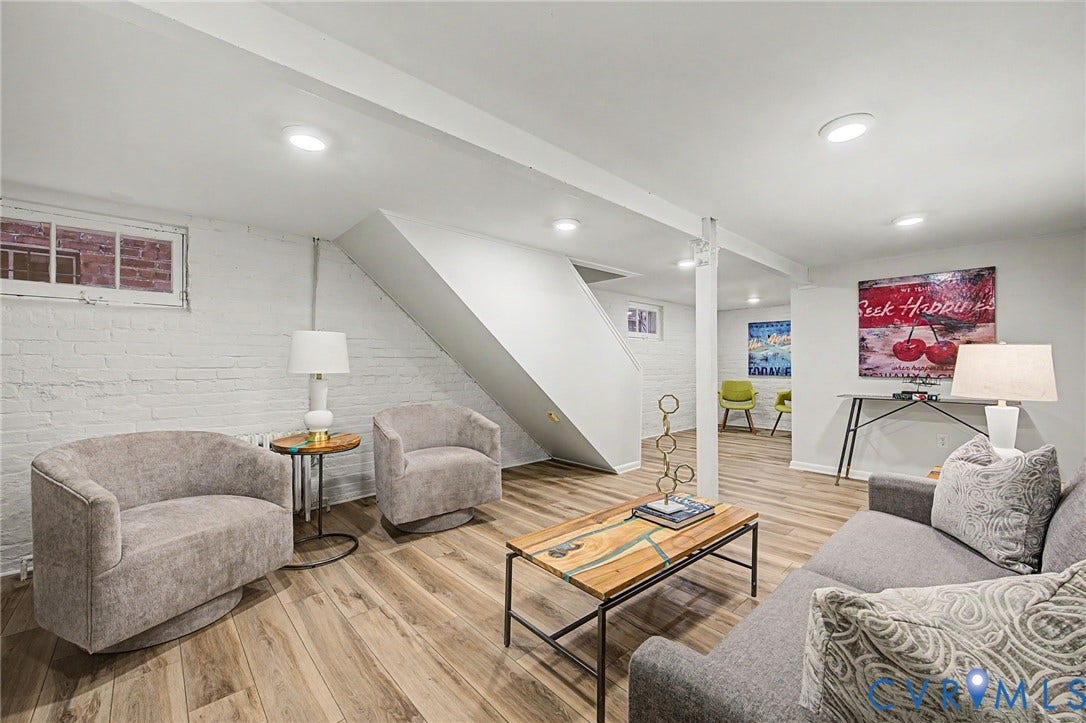 Recessed lighting illuminates the wood-finish flooring, white painted brick wall, and white exposed beams