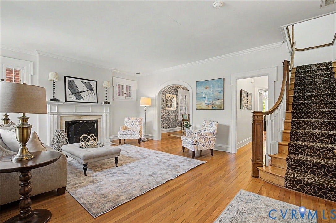 Hardwood flooring, fireplace with stone surround, archway entry, crown molding, and a staircase with patterned runner