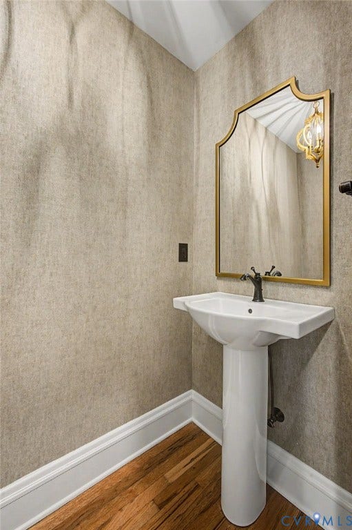 Pedestal sink with dark bronze faucet, framed mirror, textured wall covering, and wood-finish flooring