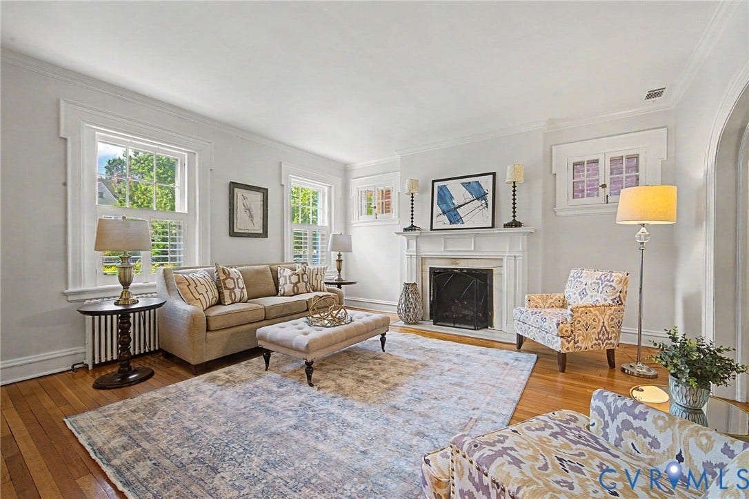Hardwood flooring, white window shutters, ornate window trim, arched entryway, and a white mantel fireplace