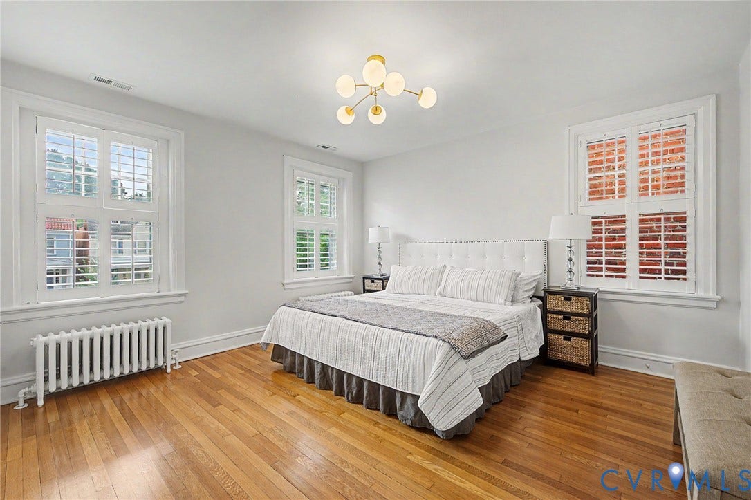 Hardwood flooring, multiple windows with white plantation shutters, white painted walls, a built-in radiator, and a modern ceiling light fixture