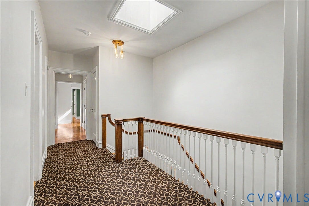 Skylight, wood banister with white spindles, overhead lighting fixture, and patterned carpet