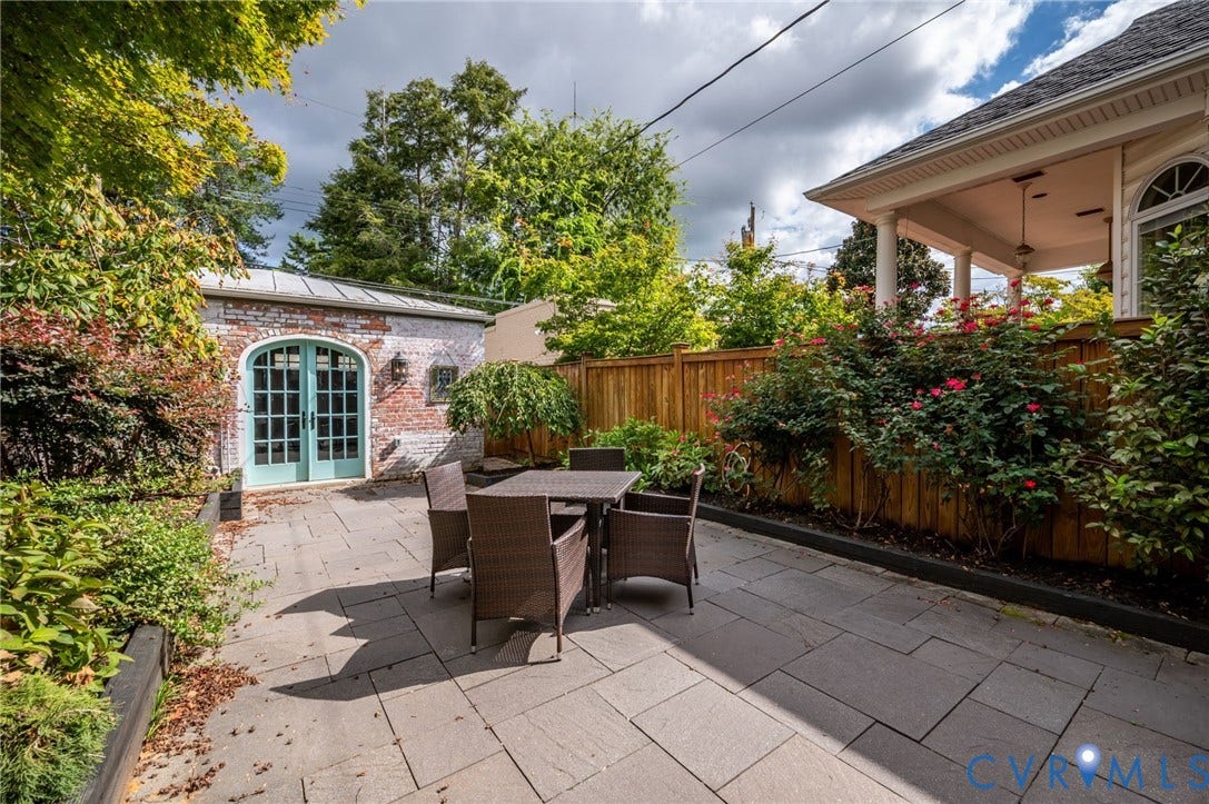 Stone paver patio featuring a white-washed brick outbuilding with arched glass-paneled doors, wood fencing, and established perimeter plantings