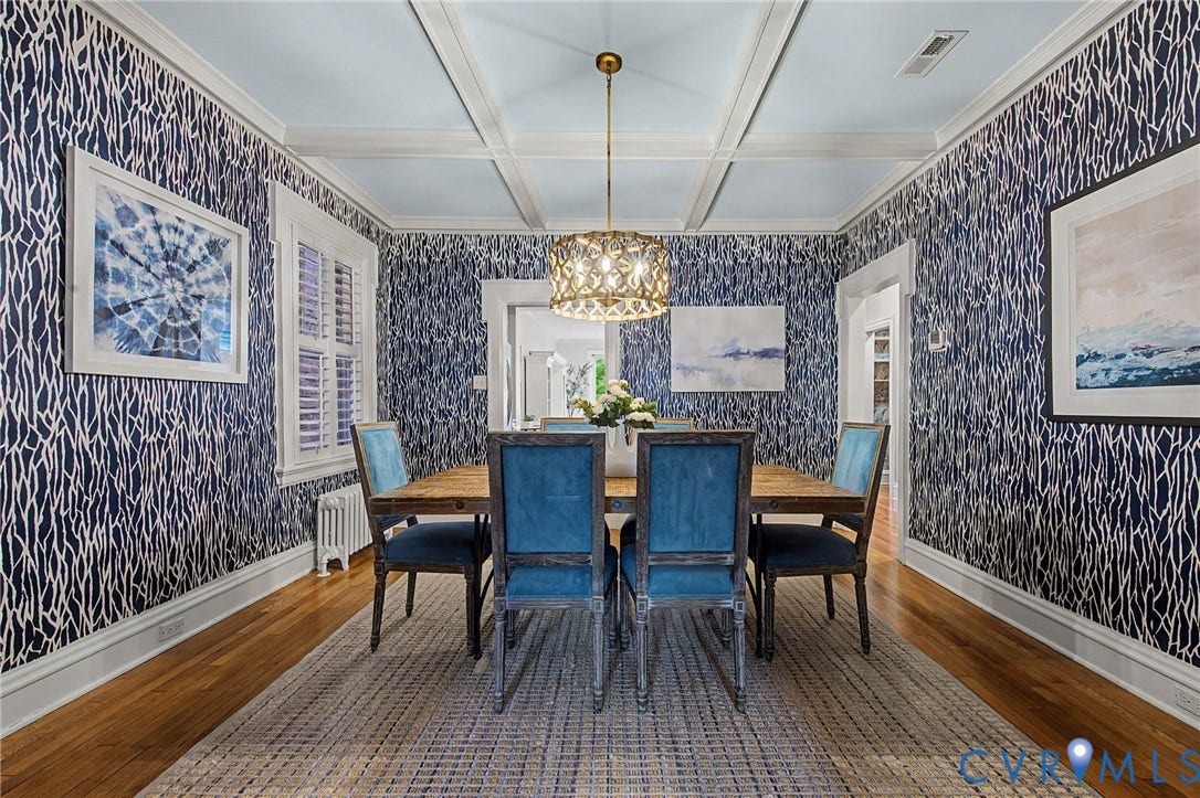 Hardwood flooring, decorative wall coverings, coffered ceiling, window with plantation shutters, and an ornate chandelier