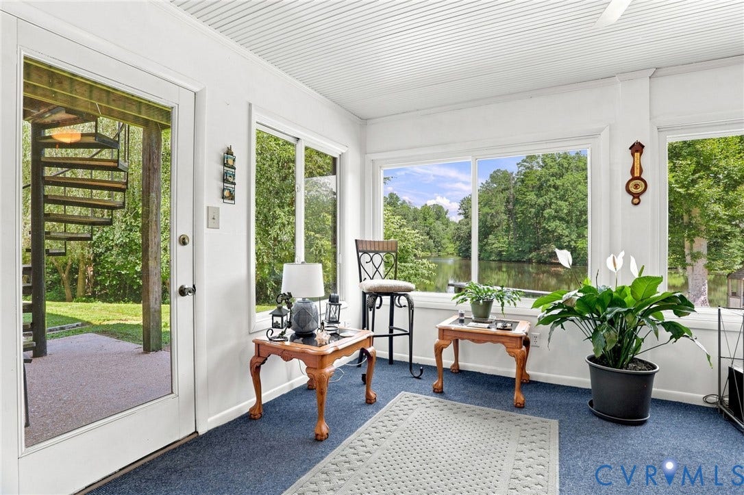 4512 Forrestal Road, Chester, VA 23831 Bright sunroom with expansive glass wall and French door access to outdoor space, featuring blue-toned wood-finish flooring, wood-trim architectural detailing, potted greenery, and abundant natural light from multiple windows overlooking mature landscaping