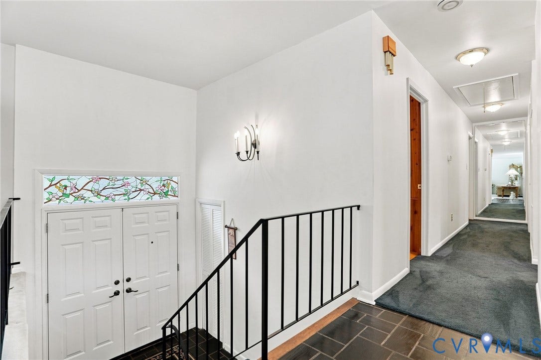 4512 Forrestal Road, Chester, VA 23831 Two-panel entry door with transom accent, slate tile flooring, wrought iron railing, wall sconce lighting, and a carpeted hallway