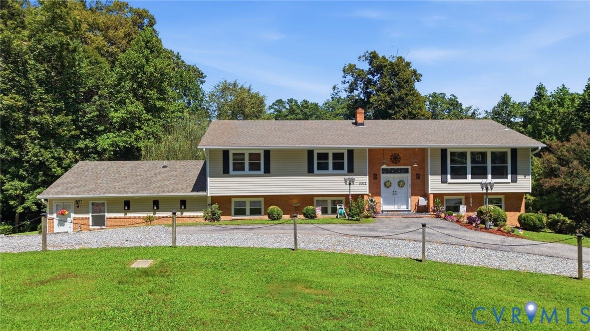 4512 Forrestal Road, Chester, VA 23831 Split-level residence featuring a brick and siding facade, dual white entry doors, black window shutters, and a gravel driveway with a chained fence