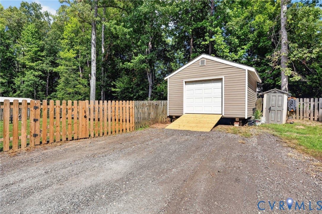 7248 Full Rack Drive, Midlothian, VA 23112 Gravel driveway, wood picket fence, tan siding storage shed with garage door, and a gray utility shed