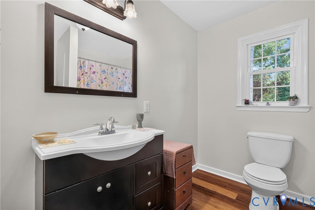 7248 Full Rack Drive, Midlothian, VA 23112 Bathroom featuring a dark wood-finish vanity with an integrated white sink, a framed mirror, a window with white trim, a toilet, and wood-finish flooring