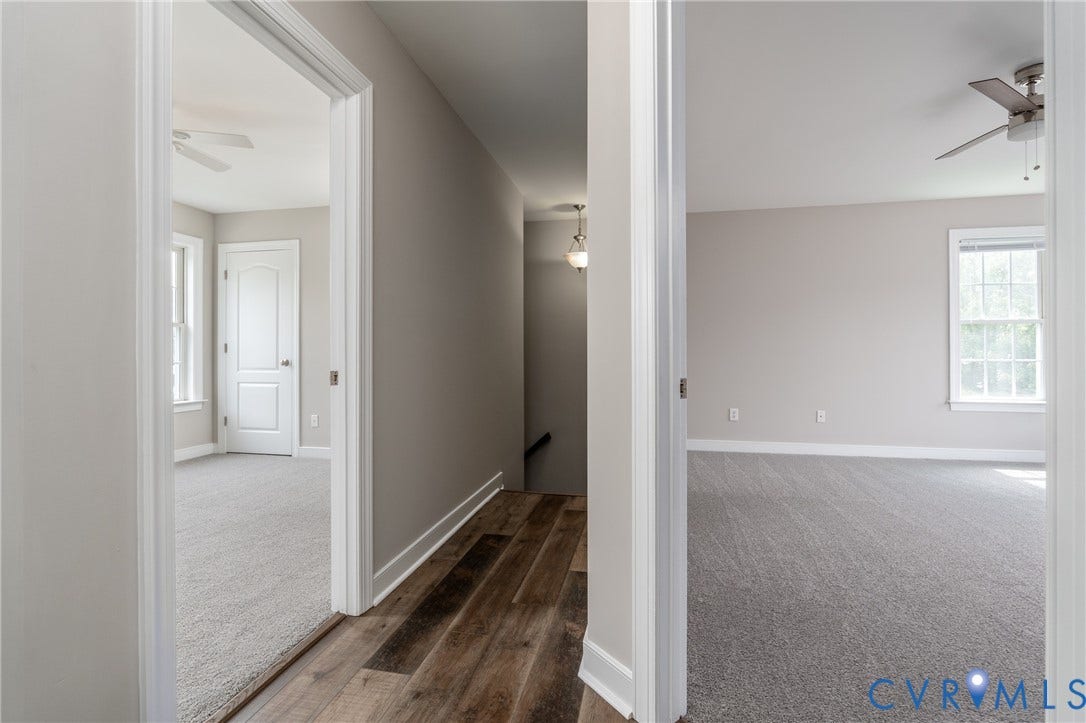Bright hallway with wood-finish flooring, white trim molding, and multiple doorways leading to carpeted rooms
