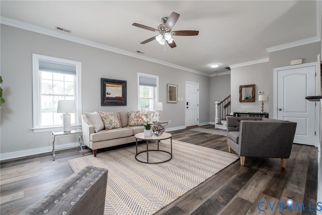 Spacious living area featuring wood-finish flooring, two large windows, crown molding, and a ceiling fan