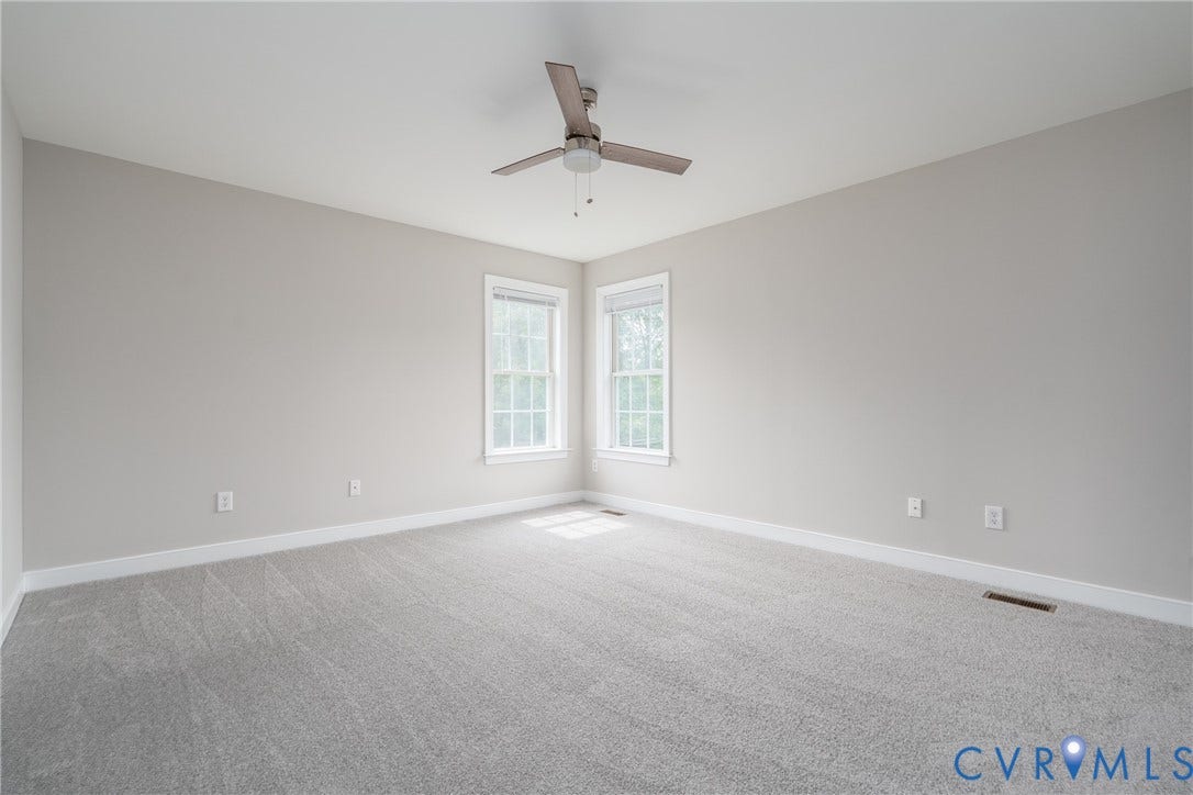Spacious room featuring gray wall-to-wall carpeting, two windows with white trim, a ceiling fan, and light gray walls