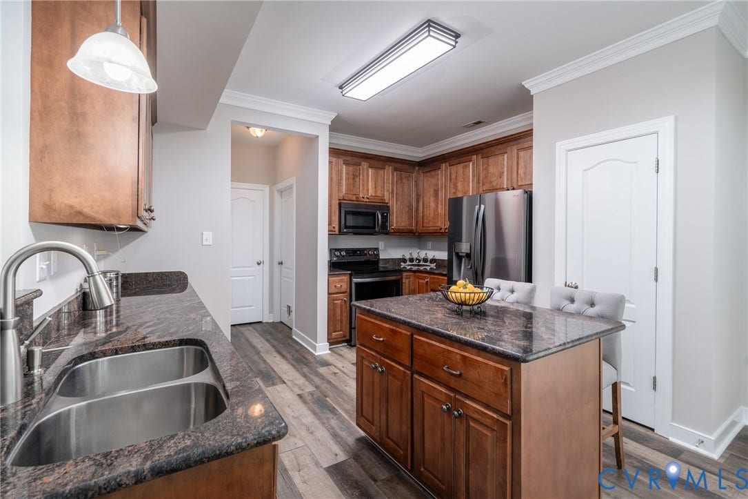 Kitchen featuring wood-finish flooring, wood cabinetry, dark countertops, a double basin stainless steel sink, and stainless steel appliances